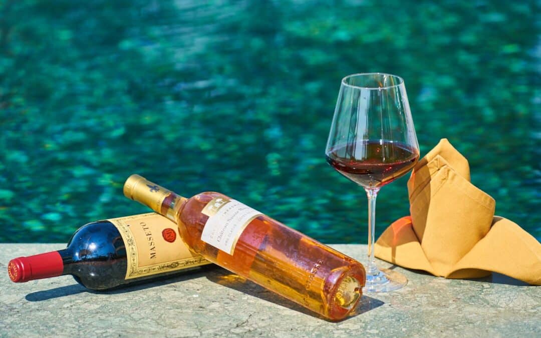 Two Labeled Bottles Of Wine Beside A Wine Glass By The Pool